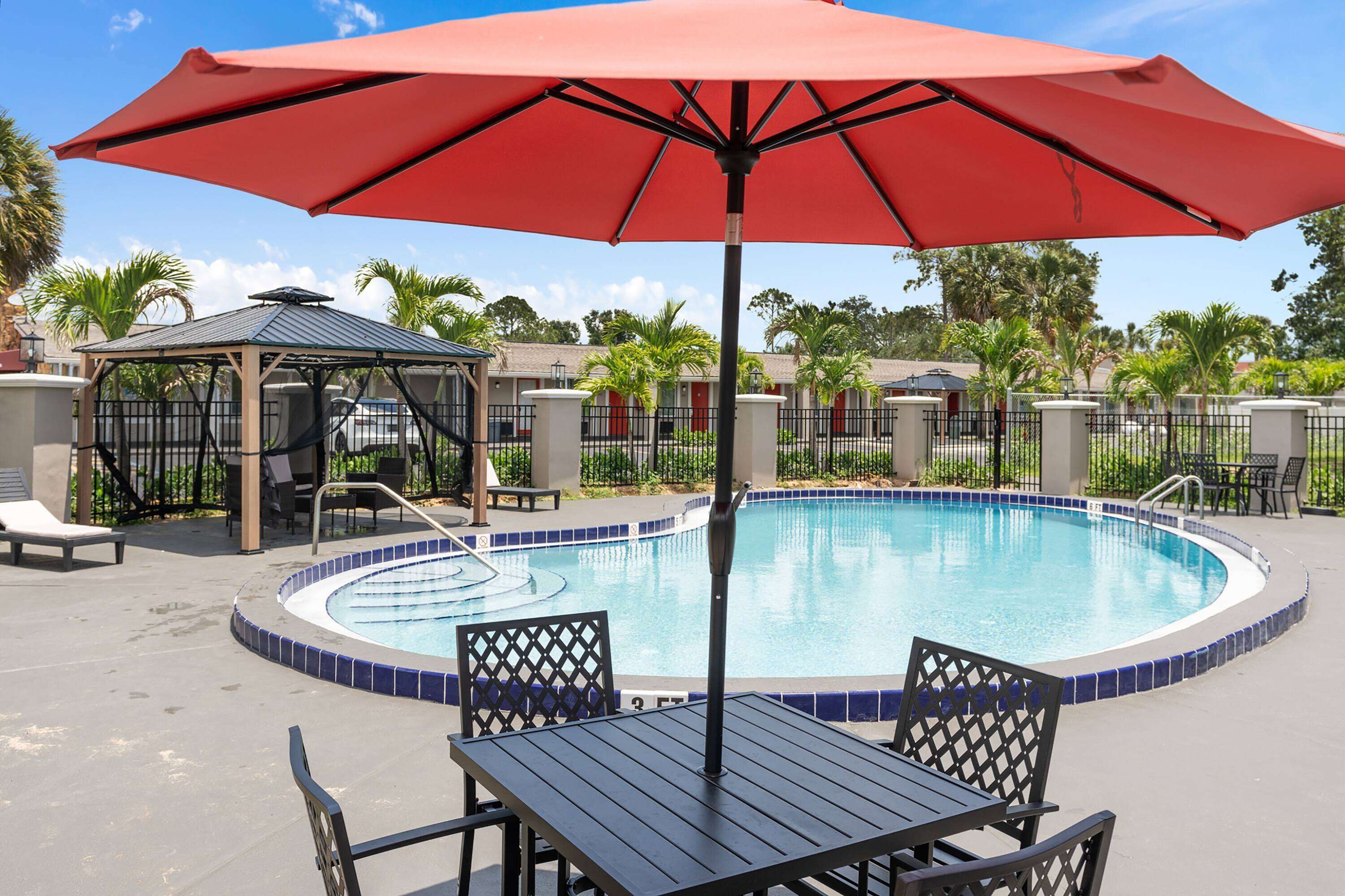 A pool area with a red umbrella, lounge chairs, and a gazebo.