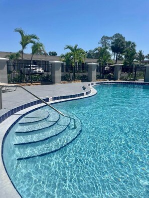 A clear swimming pool with a curved edge, surrounded by a fence and palm trees. - Super 8 by Wyndham Kissimmee/Orlando (Kissimmee)