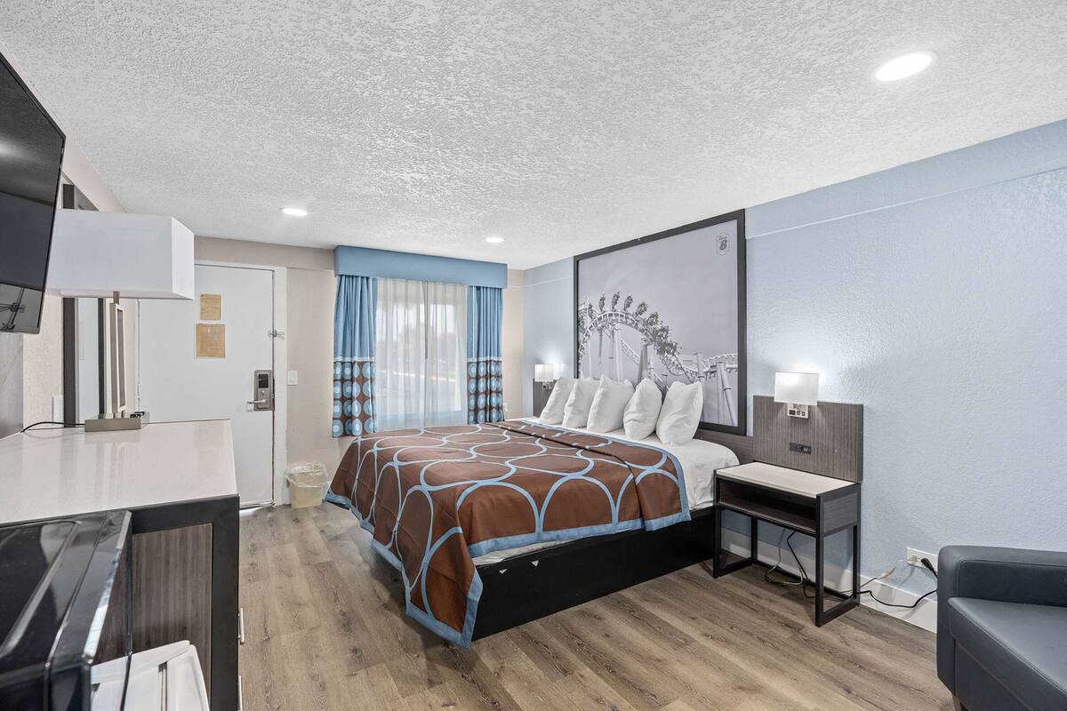 Una habitación de hotel con cama, mesita de noche, escritorio y un ventanal con cortinas.