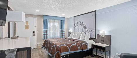A hotel room with a bed, bedside table, desk, and a large window with curtains.