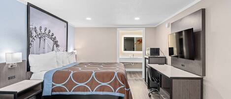 A modern hotel room with a large bed, a desk, a TV, and a bathroom visible through an open door.