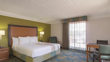 Une chambre d’hôtel avec un lit, un bureau, une chaise, une lampe et une fenêtre avec des rideaux.