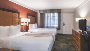 Una habitación de hotel con dos camas, televisor, escritorio y cómoda.