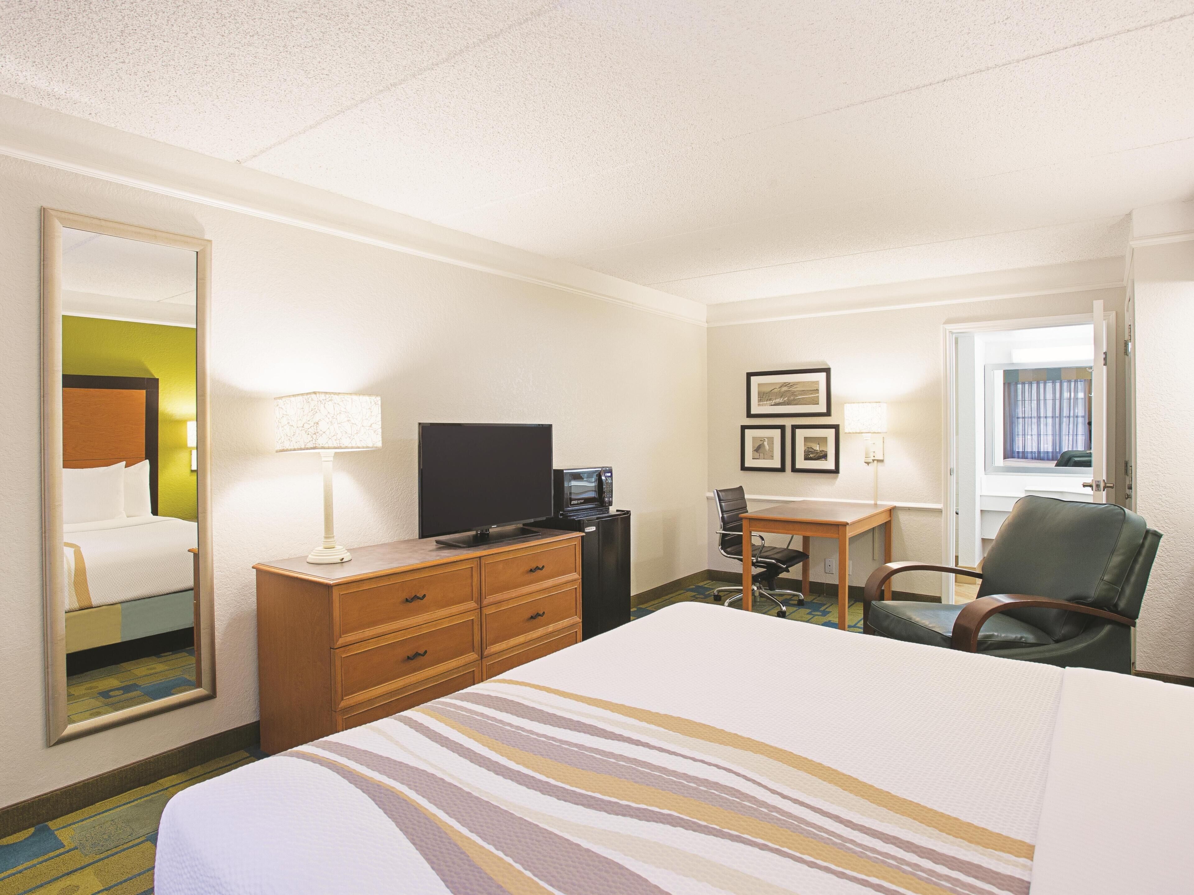Une chambre d’hôtel équipée d’un lit, d’un bureau, d’une chaise, d’une télévision, d’une commode et d’un miroir.