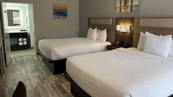 A hotel room with two beds, a desk, and a bathroom visible through an open door.