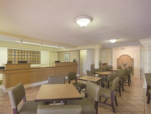 Un restaurante con una recepción, varias mesas y sillas, y una pared decorativa.