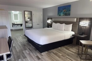 Habitación de hotel con una cama grande, mesitas de noche, un escritorio, una silla, un espejo y un cuadro en la pared.