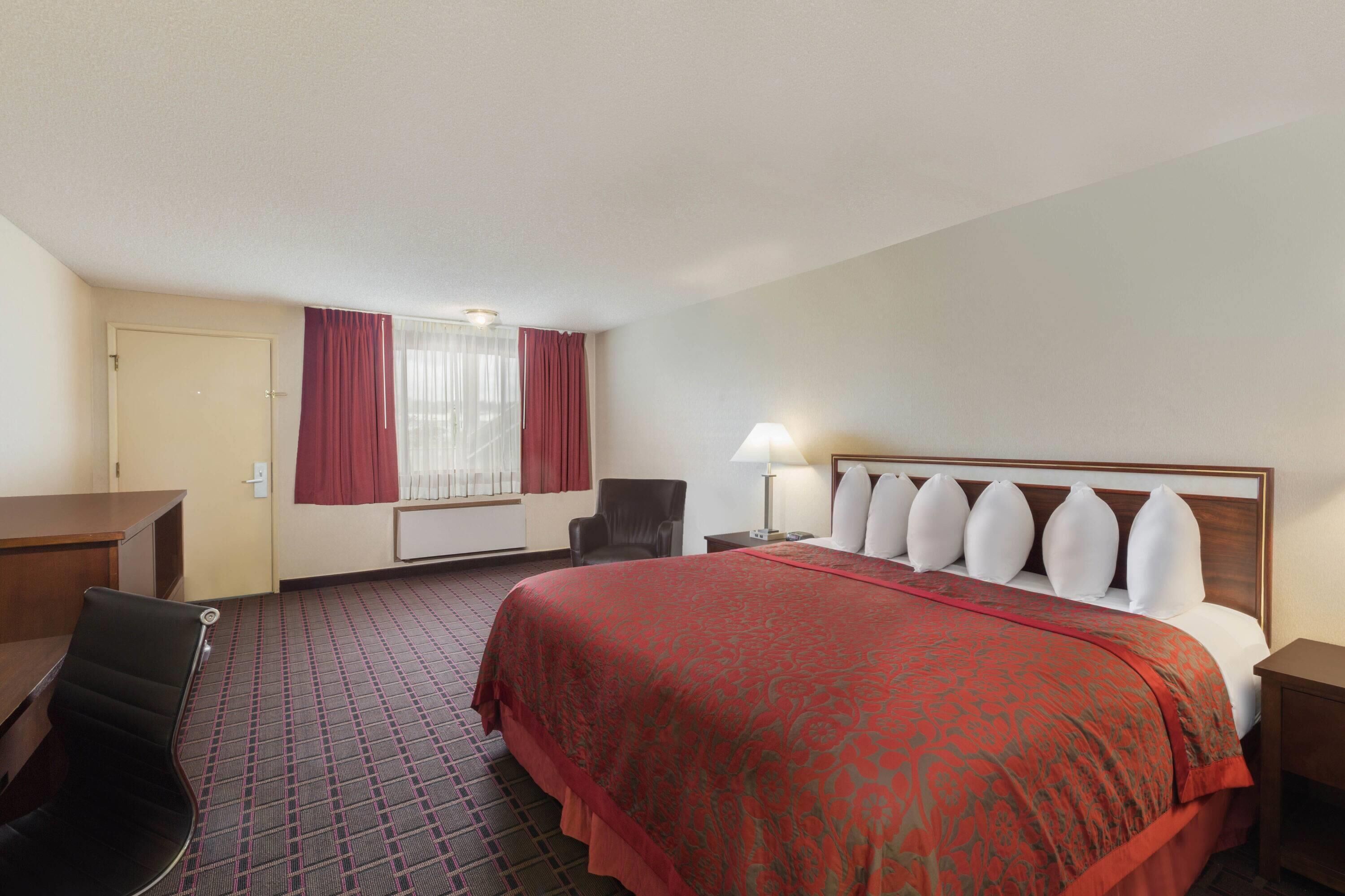 A hotel room with a large bed, a desk, a chair, and a window with curtains.