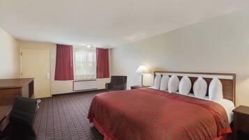 Una habitación de hotel con una cama grande, un escritorio, una silla y un ventanal con cortinas.