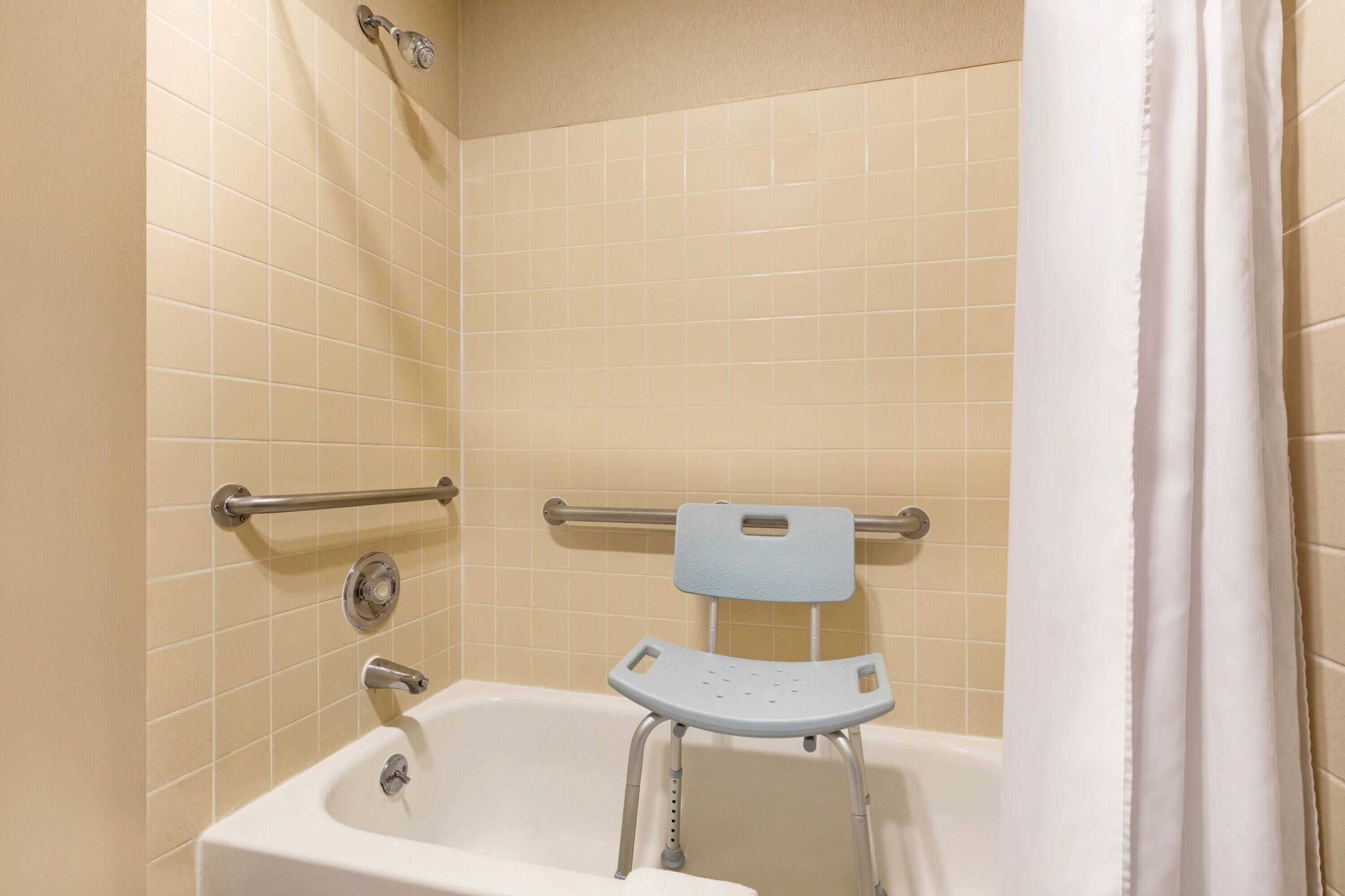 A bathroom with a bathtub, grab bars, and a shower curtain.