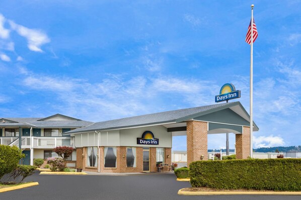 A Days Inn with a covered entrance, a parking lot, and a flagpole with an American flag. - Days Inn by Wyndham Auburn (Auburn)