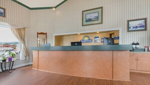 A reception desk with a Days Inn sign, a framed picture, and a window with curtains. - Days Inn by Wyndham Auburn (Auburn)