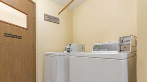 A laundry area with two white washing machines, a wooden door labeled "EMPLOYEES ONLY", and a sign on the wall. - Days Inn by Wyndham Auburn (Auburn)