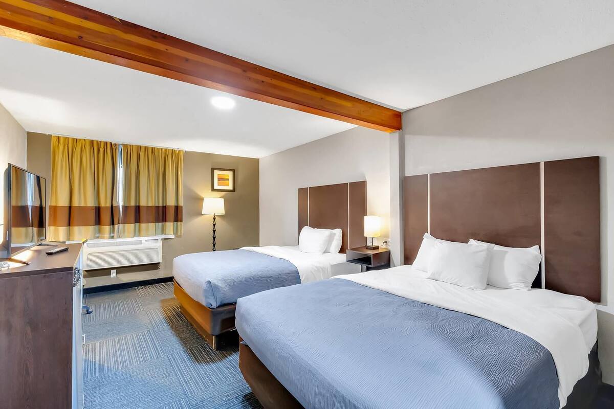 Habitación de hotel con dos camas, un escritorio, una lámpara y una ventana con cortinas.
