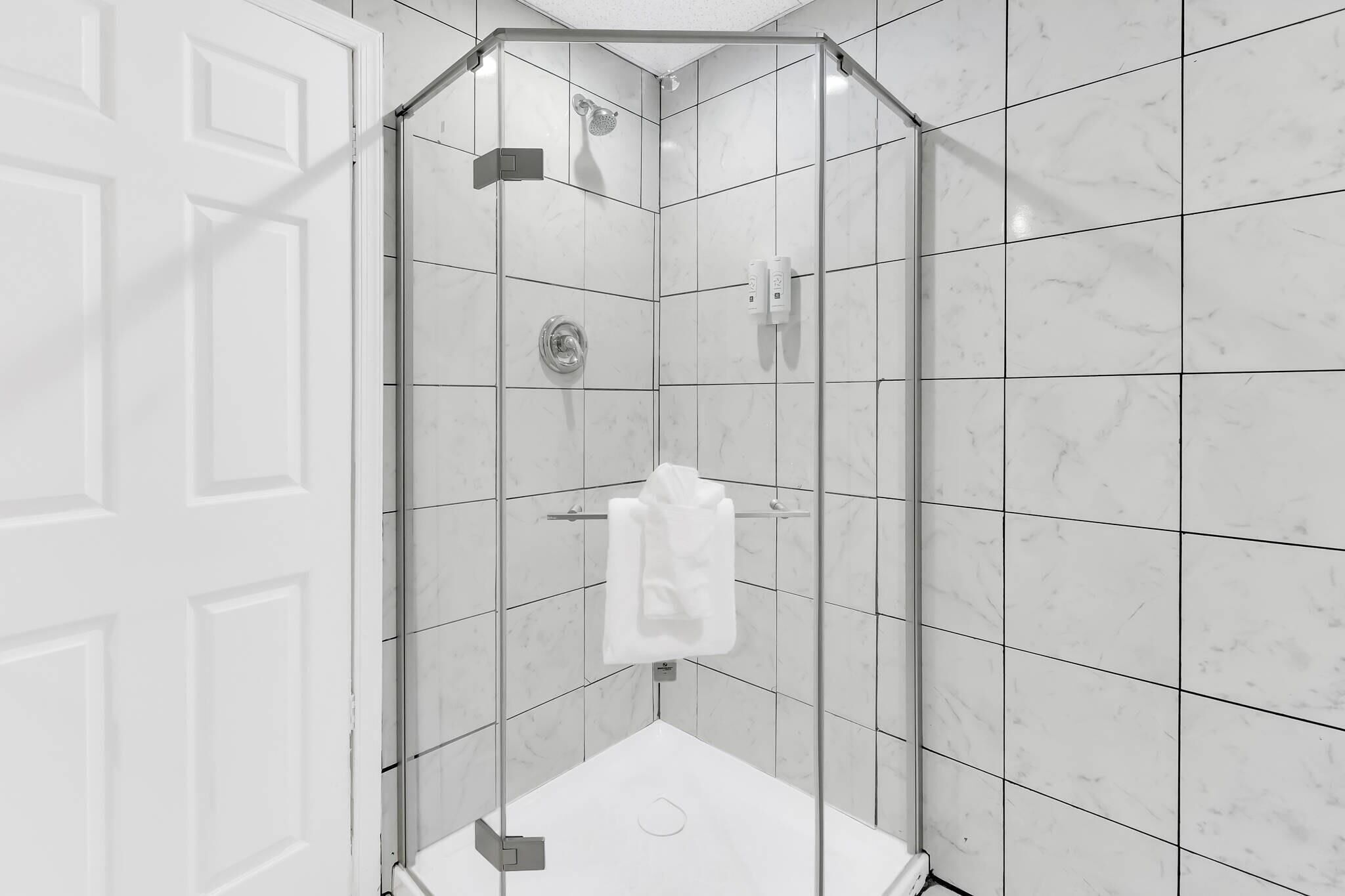 Une salle de bain moderne avec une douche à parois de verre, des carreaux de marbre blanc et une serviette blanche suspendue à un porte-serviettes.