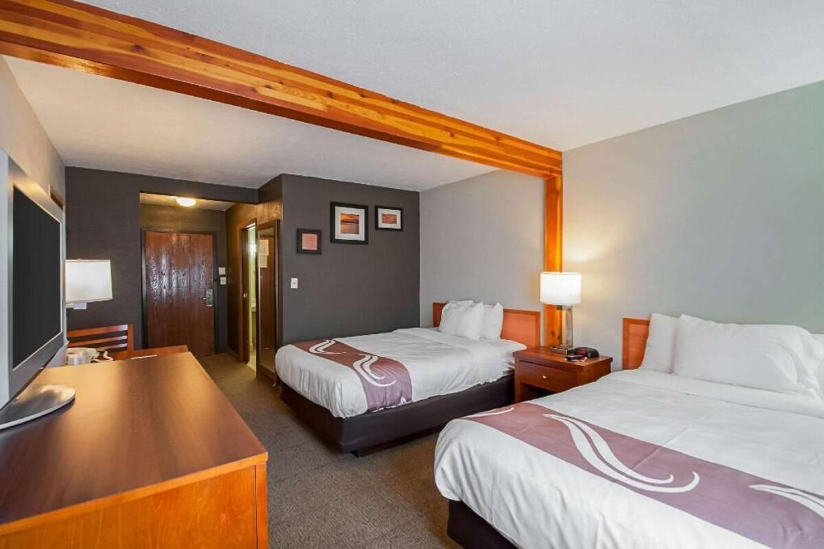 Habitación de hotel con dos camas, un escritorio, un televisor y una viga de techo de madera.