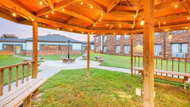 A covered outdoor area with wooden beams and string lights, picnic tables, and a brick building in the background. - Quality Inn Salisbury North (Salisbury)