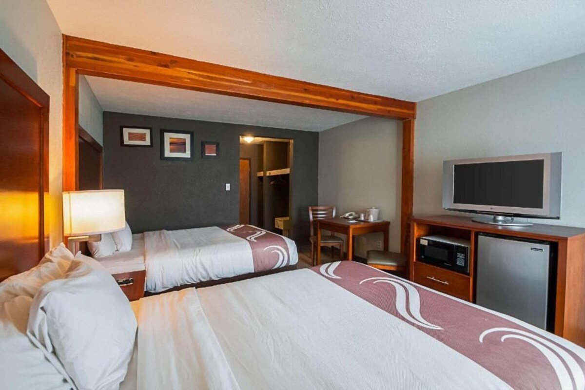 Quarto de hotel com duas camas, uma escrivaninha, televisão e frigorífico.