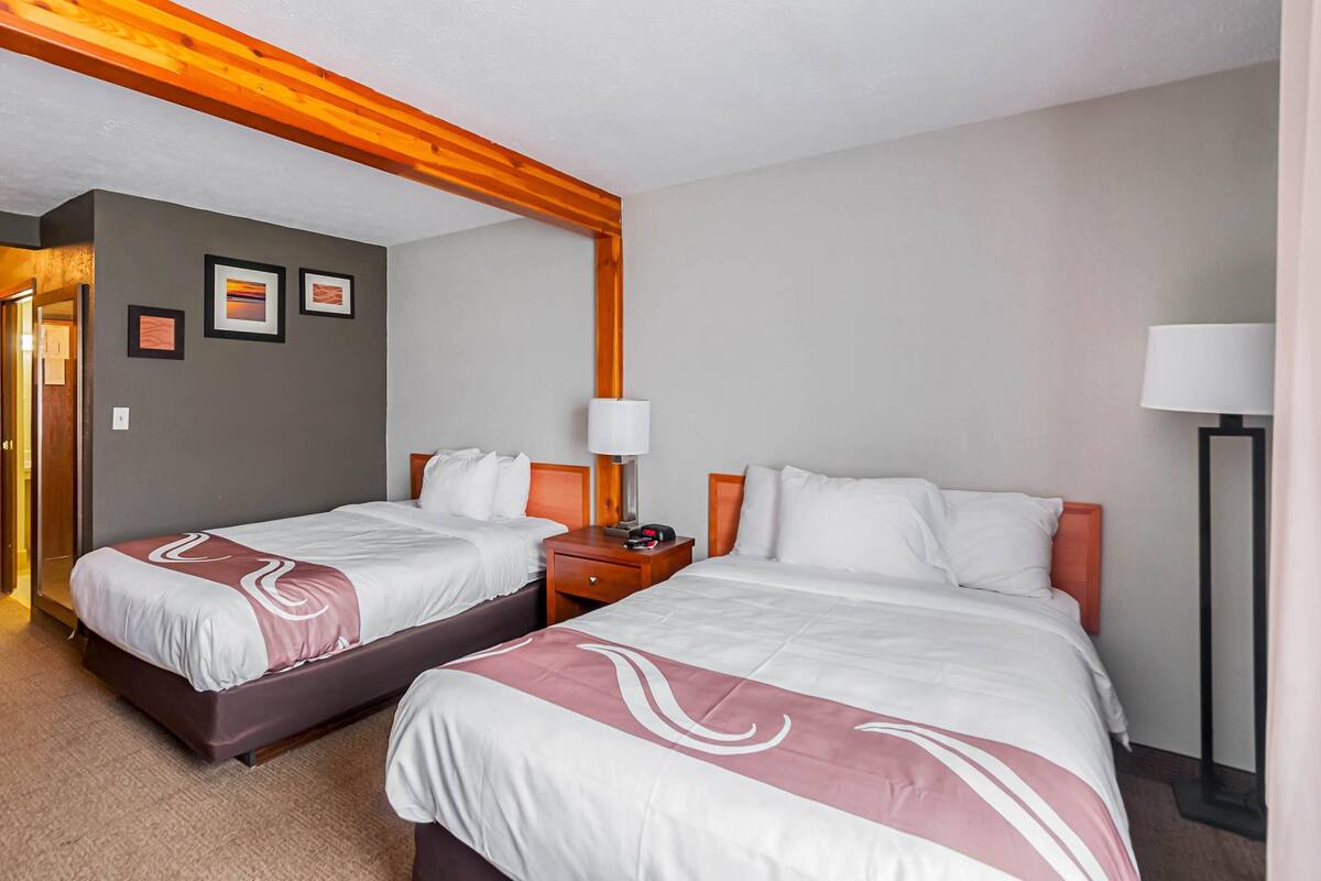 Habitación de hotel con dos camas, techo de madera, mesita de noche con lámpara y cuadros en la pared.