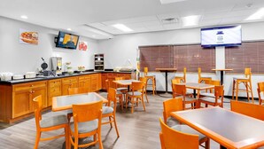 A modern dining area with wooden tables and chairs, a kitchen counter with appliances, and a television mounted on the wall. - Quality Inn Salisbury North (Salisbury)