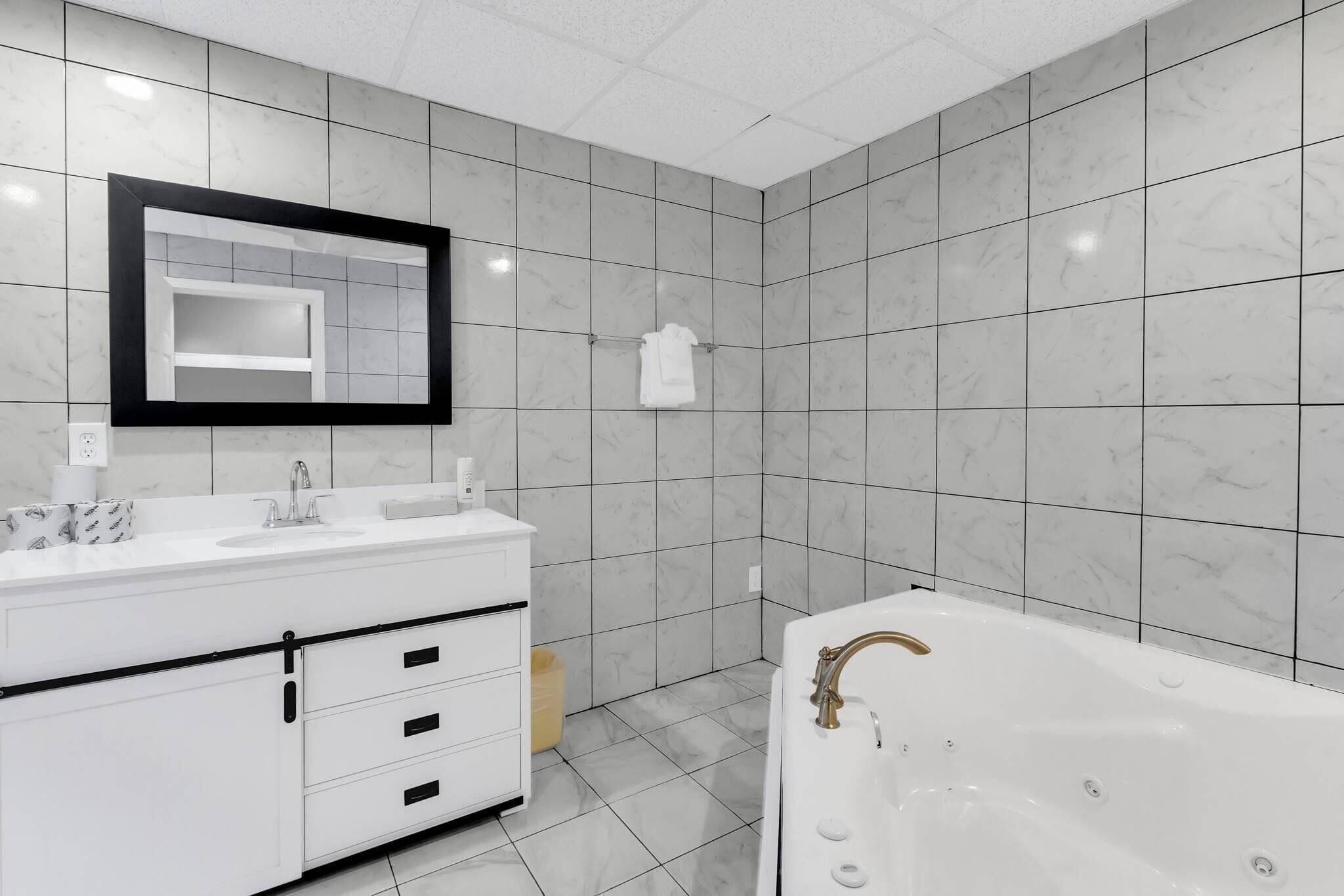 Une salle de bain moderne avec un meuble-lavabo blanc, un grand miroir, une baignoire et des carreaux de marbre gris.
