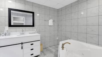 Une salle de bain moderne avec un meuble-lavabo blanc, un grand miroir, une baignoire et des carreaux de marbre gris.