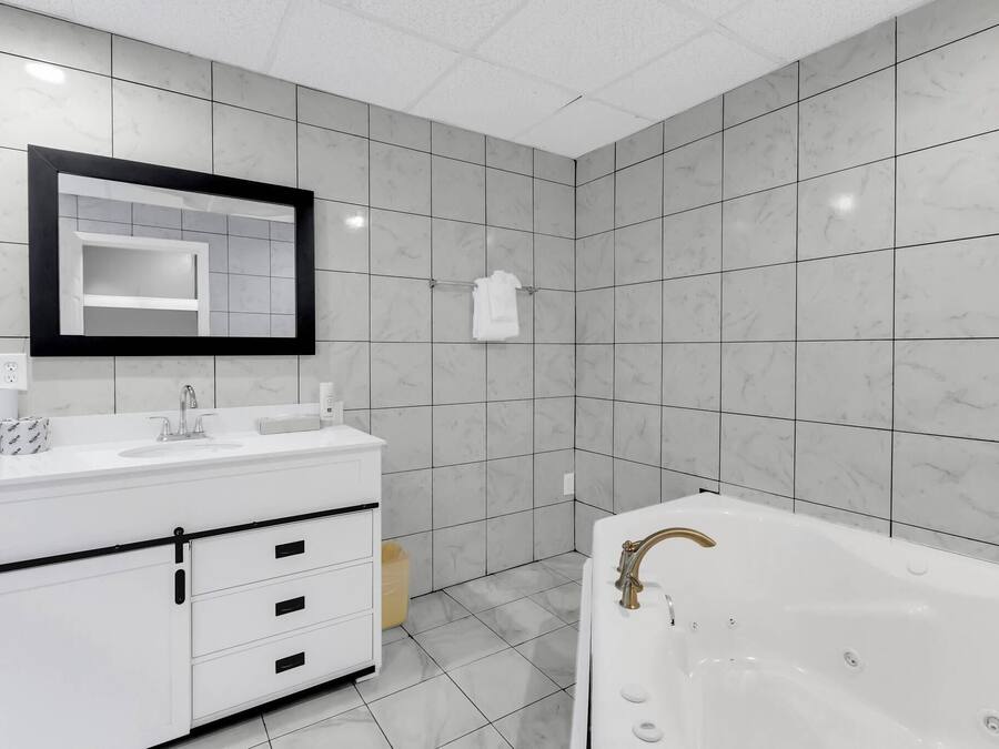 Une salle de bain moderne avec un meuble-lavabo blanc, un grand miroir, une baignoire et des carreaux de marbre gris.