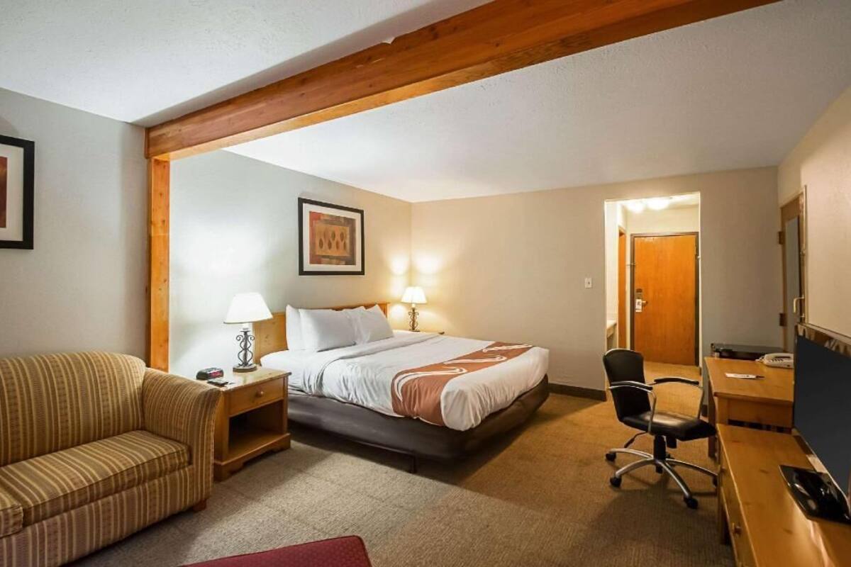 Habitación de hotel con cama, escritorio, silla, sofá y viga de techo de madera.