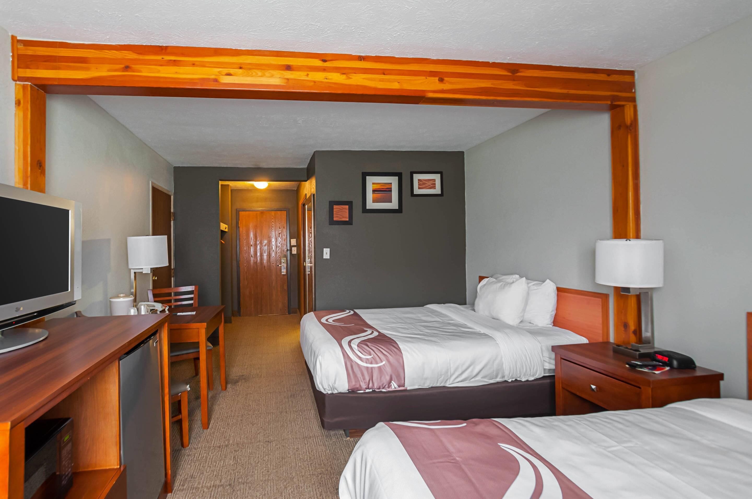 Ein Hotelzimmer mit zwei Betten, einem Schreibtisch mit Fernseher und einer Holzbalkendecke.
