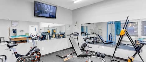 A gym with exercise equipment, a television, and a mirror.