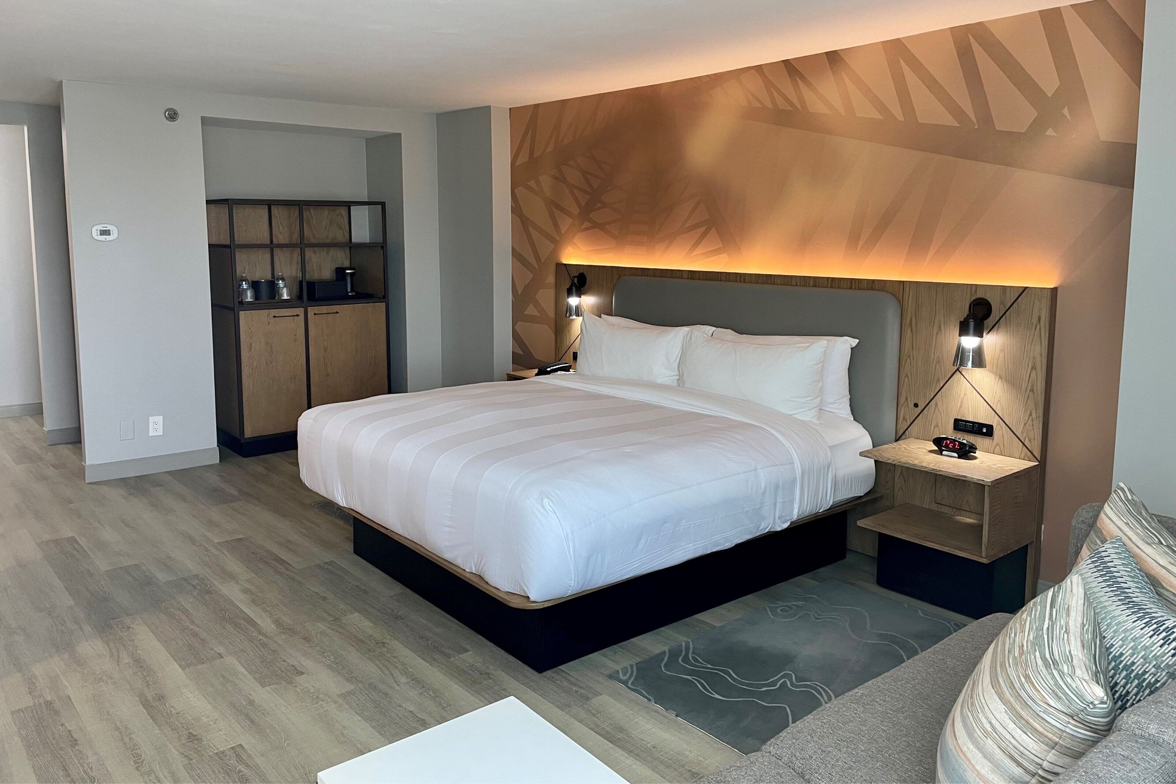 Una habitación de hotel moderna con una cama grande, mesitas de noche, un armario y un diseño de techo original.