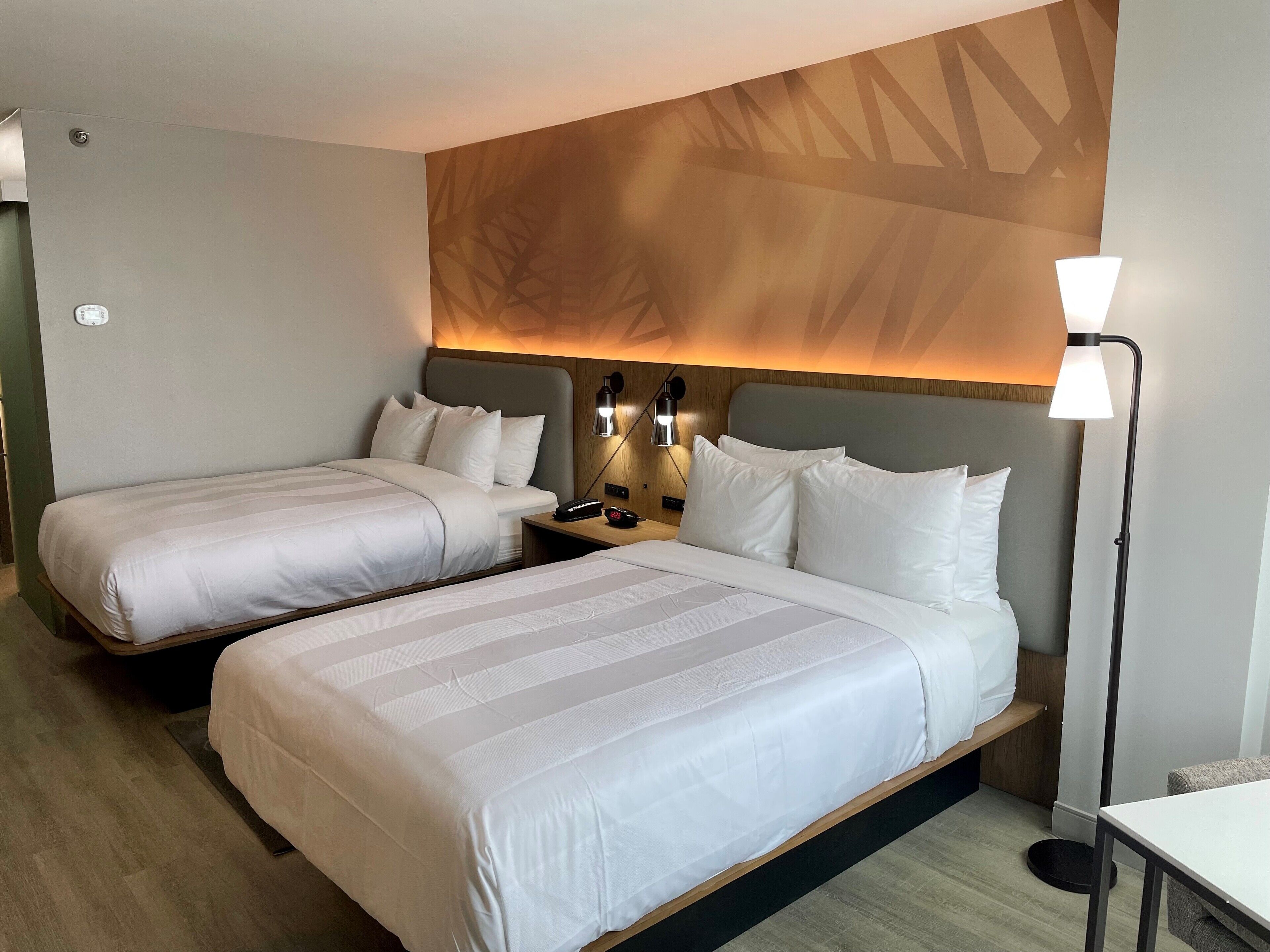 Ett hotellrum med två sängar, ett nattduksbord, en lampa och en väggmonterad lamparmatur.
