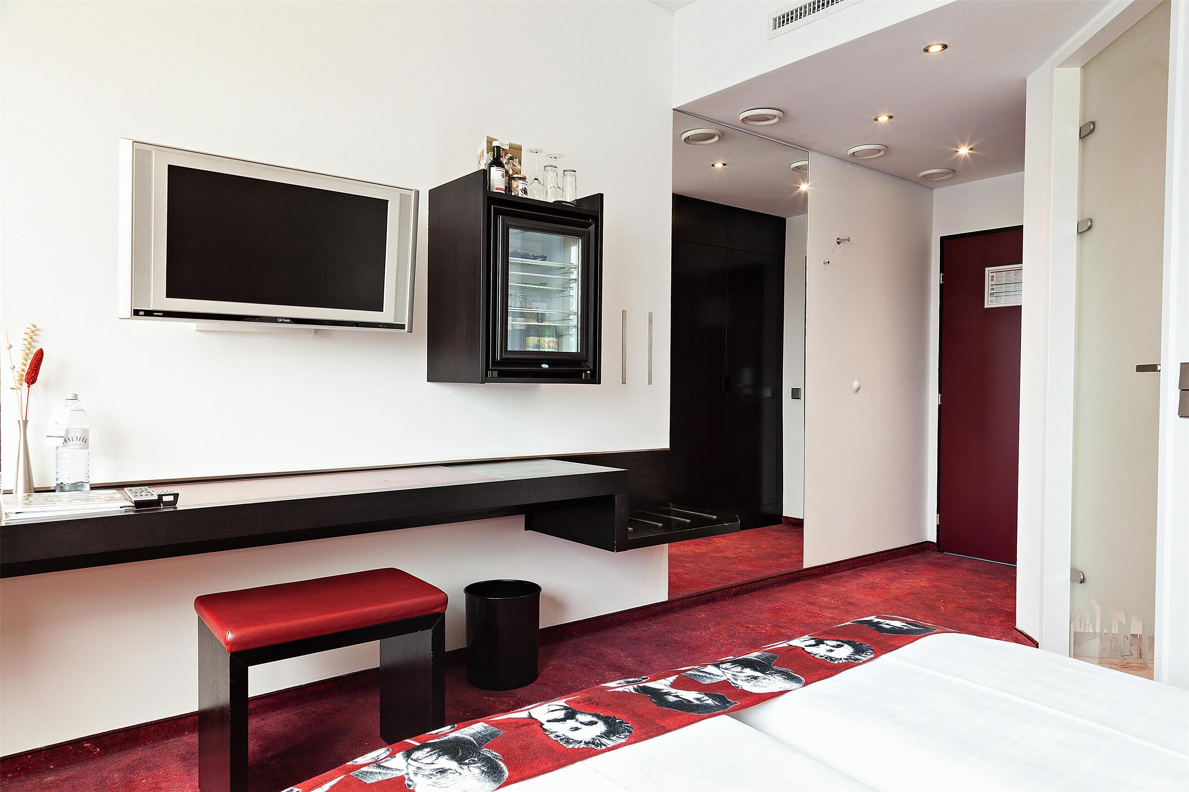Una habitación de hotel moderna con una cama grande, un escritorio con una silla, un televisor y un mini bar.