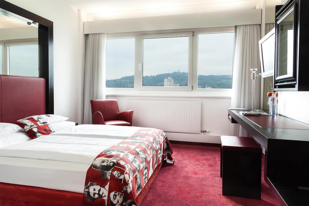 A hotel room with a large bed, a desk, a chair, and a view of the city.