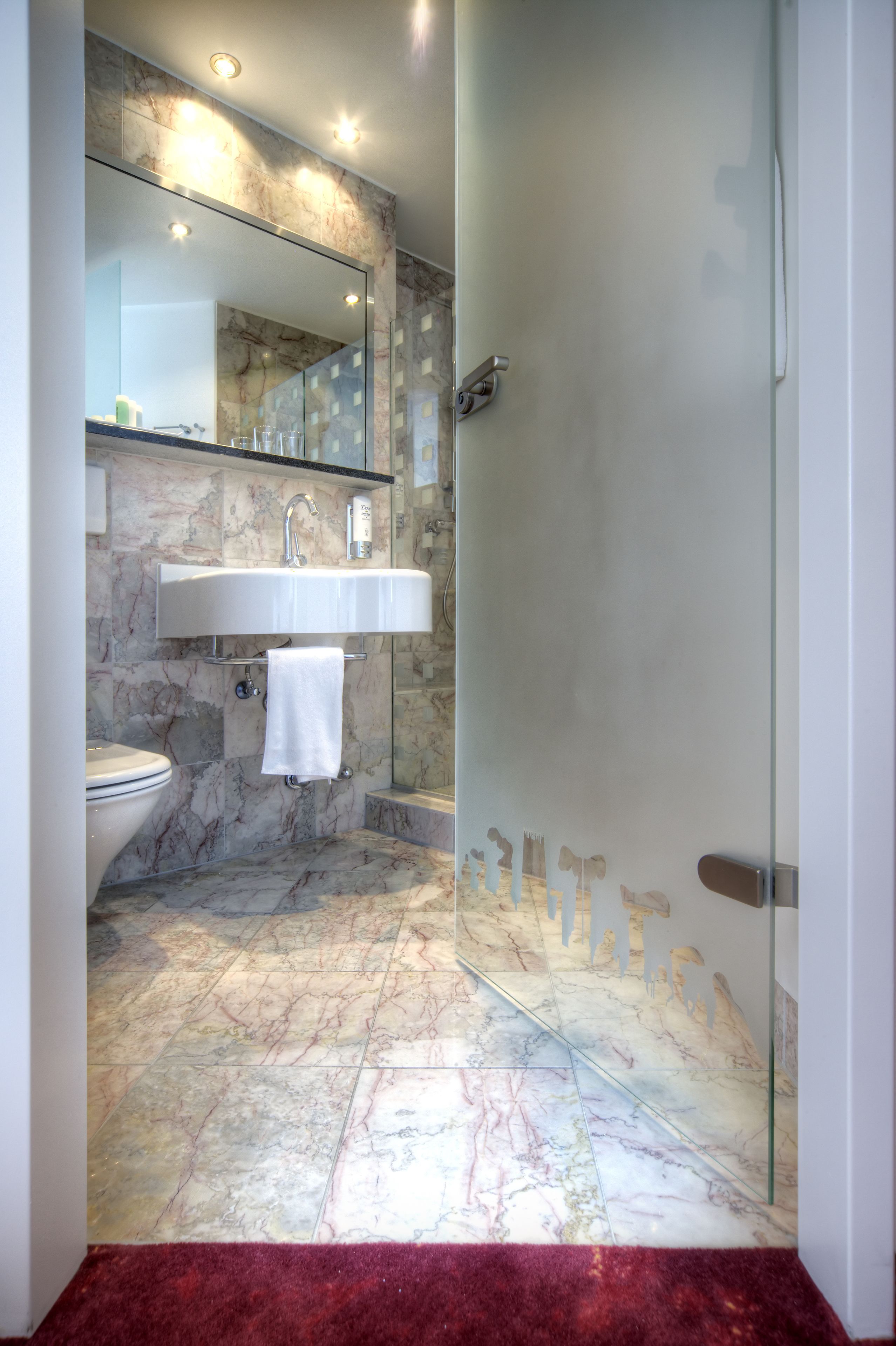 A modern bathroom with a marble floor, a glass shower enclosure, and a white sink.