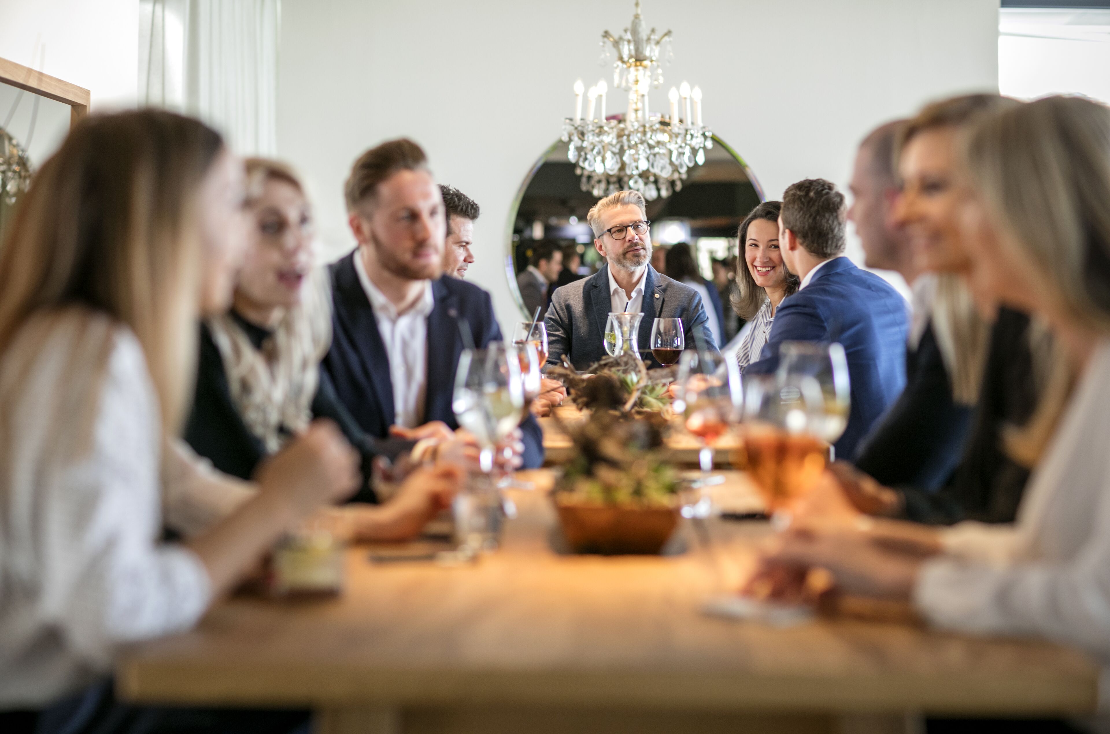 Un grupo de personas sentadas alrededor de una mesa, con copas de vino y una decoración central.