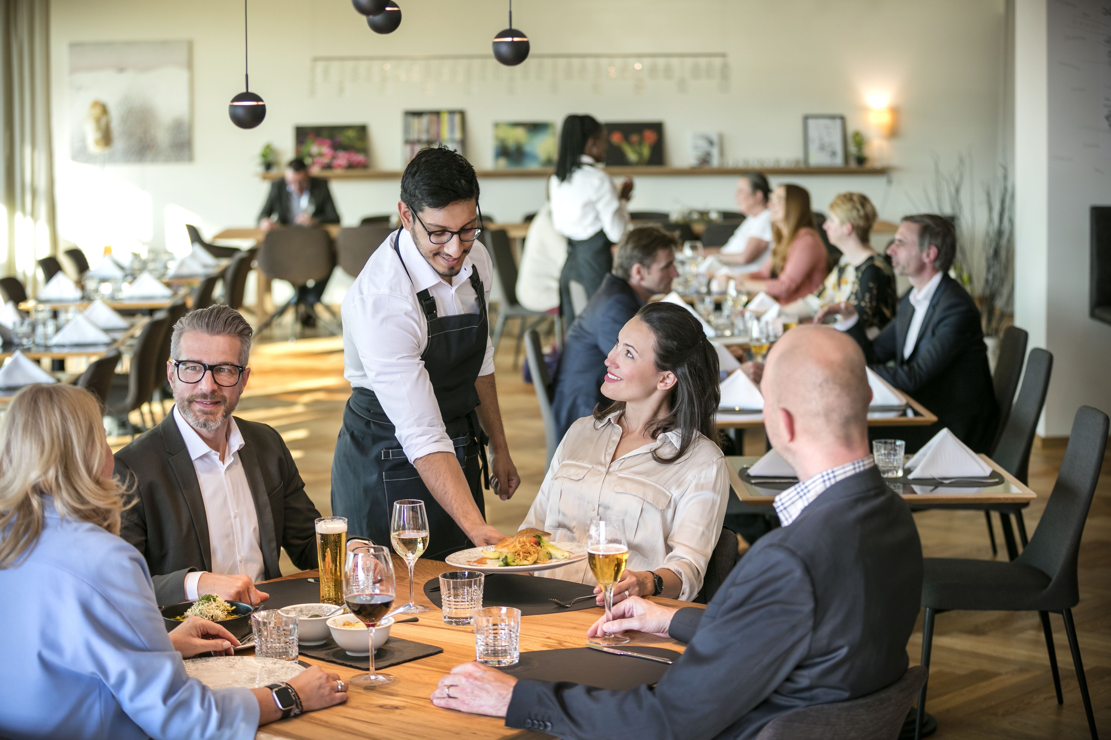 A restaurant with multiple tables, waitstaff, and diners.