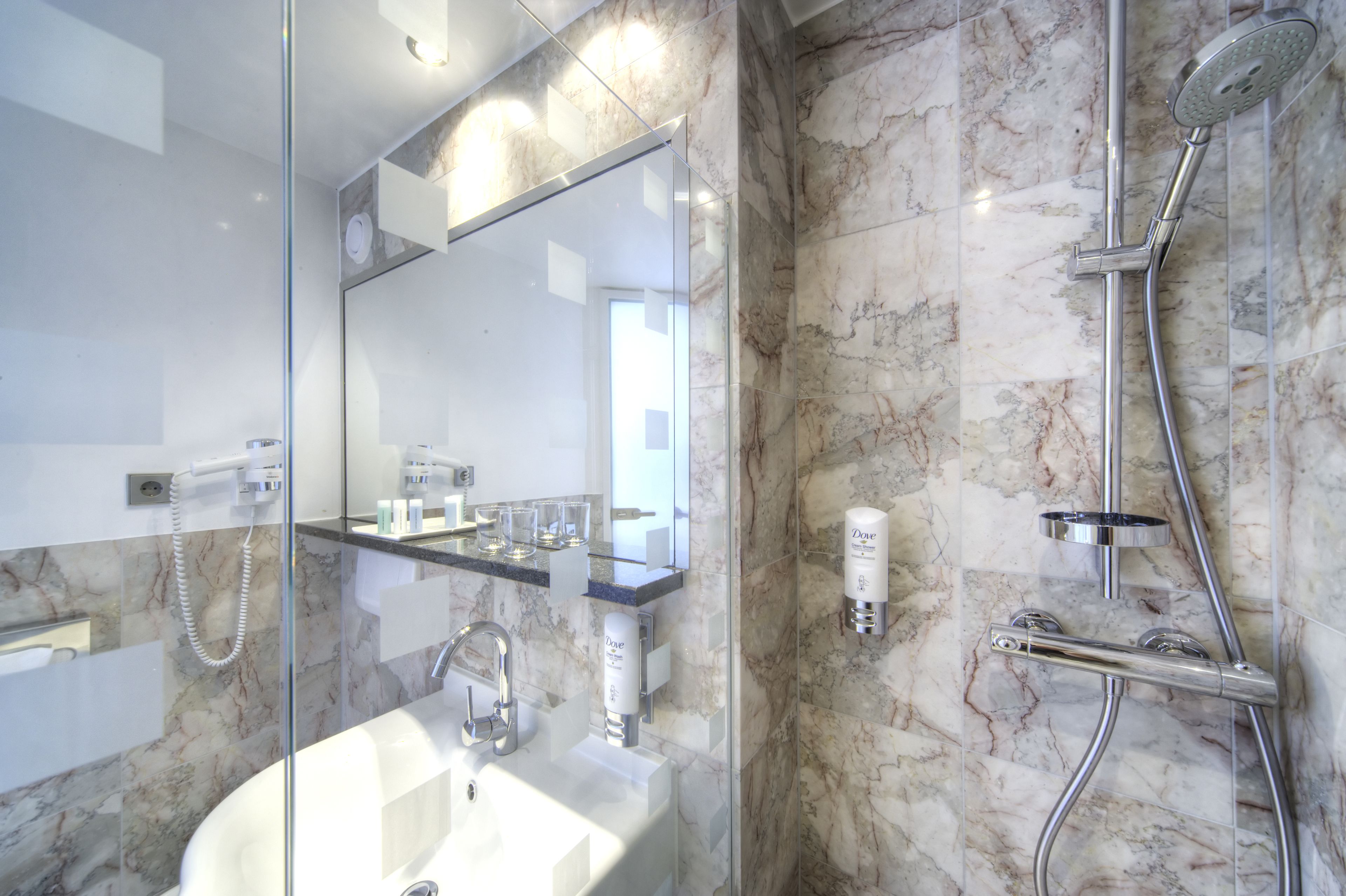 Un baño moderno con ducha de vidrio, pared con azulejos de mármol y lavamanos empotrado.