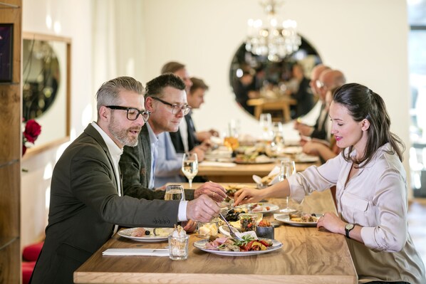 A group of people dining at a wooden table in a well-lit restaurant with a chandelier.