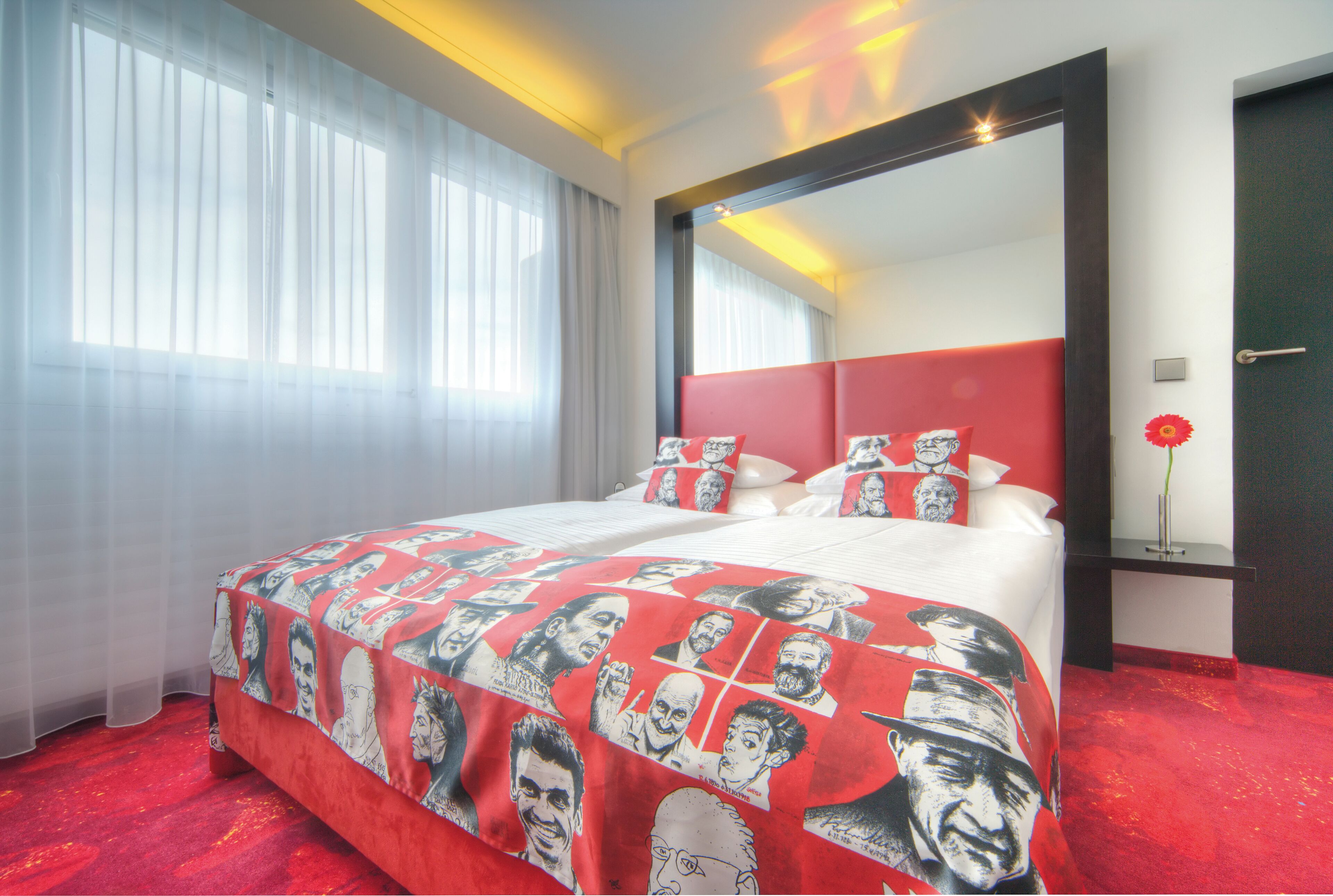 A hotel room with a large bed, a red and white headboard, a mirror, and a red carpet.
