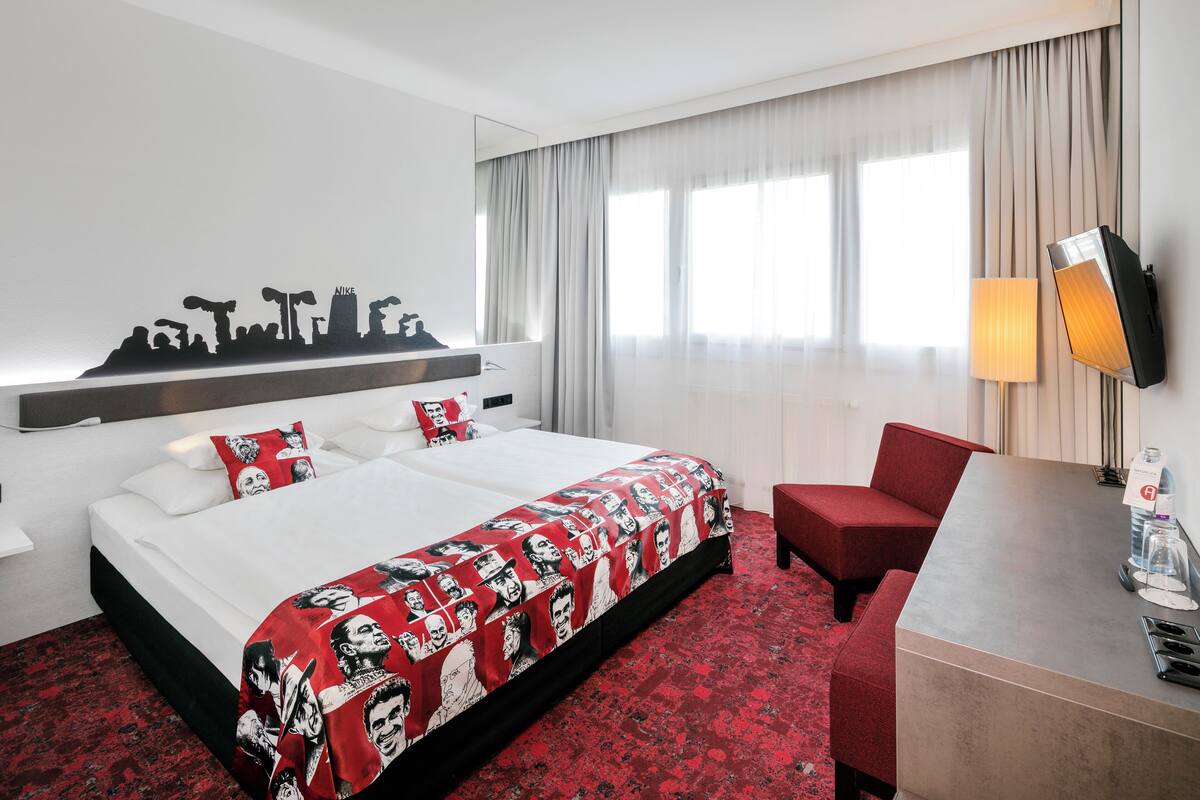 A hotel room with a bed, a desk, a chair, a mirror, and a window with curtains.