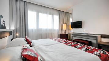 Camera d'albergo con due letti, una scrivania, una TV a schermo piatto, una lampada e vista sulla città.