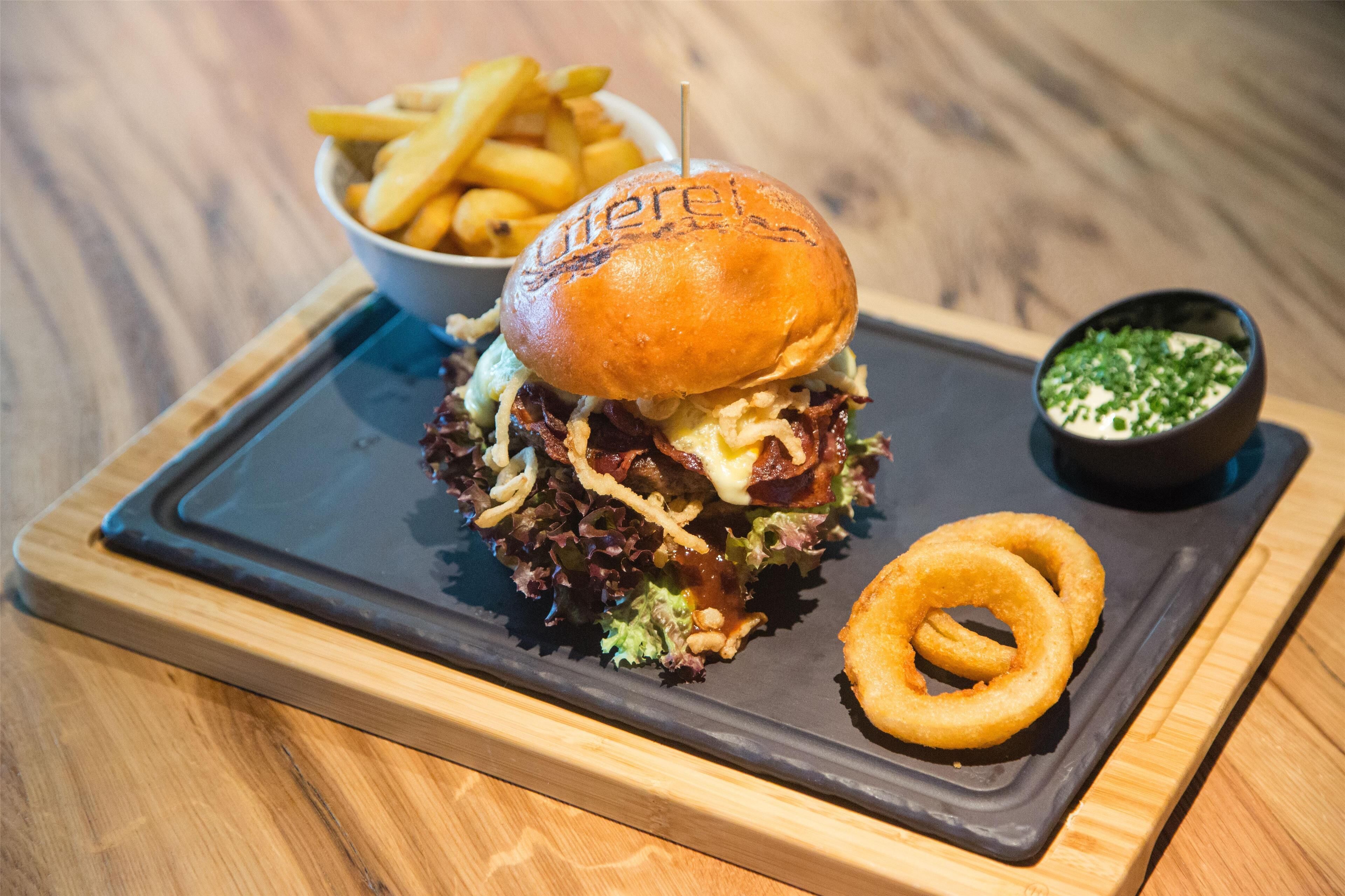 Ein Burger mit einem Brötchen mit dem Aufdruck "Burger King“, dazu Pommes und eine kleine Schüssel mit Zwiebelringen auf einem Holztisch.