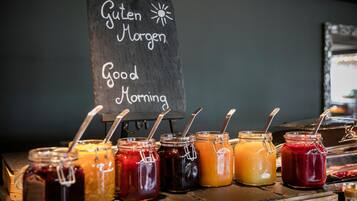 Una barra de desayuno con un letrero de pizarra que dice 'Guten Morgen Good Morning' y varios frascos de mermeladas y conservas.