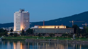 A hotel with a modern design, a large glass facade, and a view of a body of water. - ARCOTEL Nike (Linz)