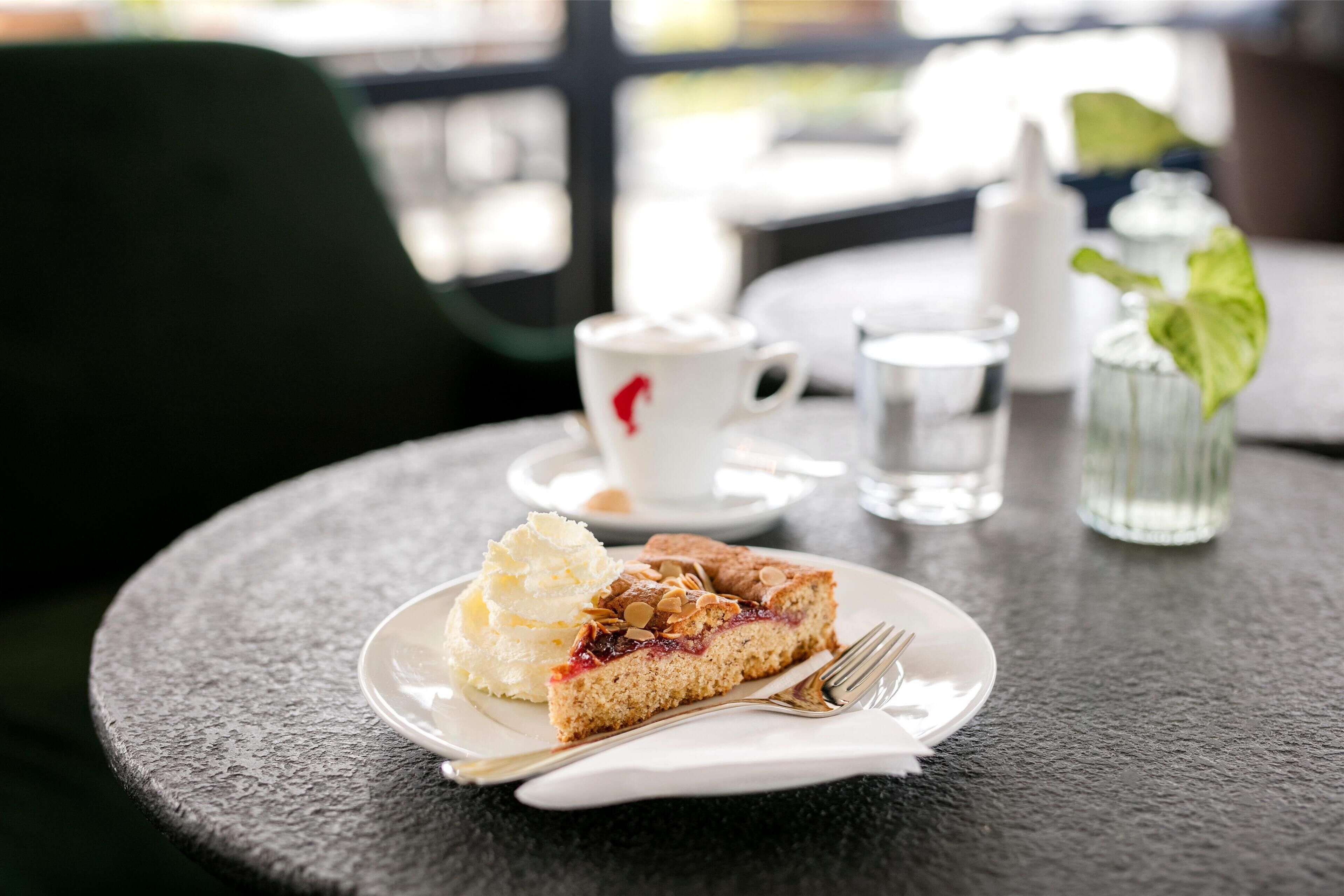A slice of cake with whipped cream on a plate, a cup of coffee, and a glass of water on a table.