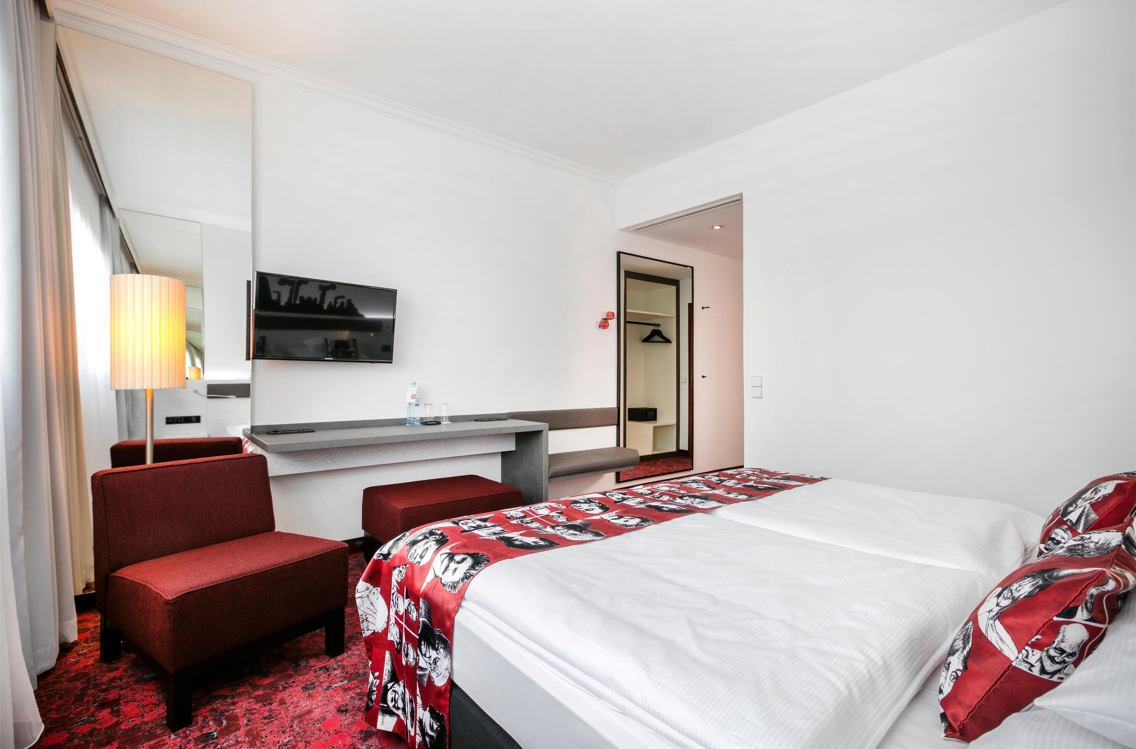 Una camera d'albergo con un letto, una scrivania, una sedia, una televisione e uno specchio.