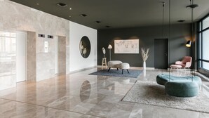 A modern lobby with a marble floor, a round mirror, a seating area with a sofa and ottoman, and a large window with natural light. - ARCOTEL Nike (Linz)