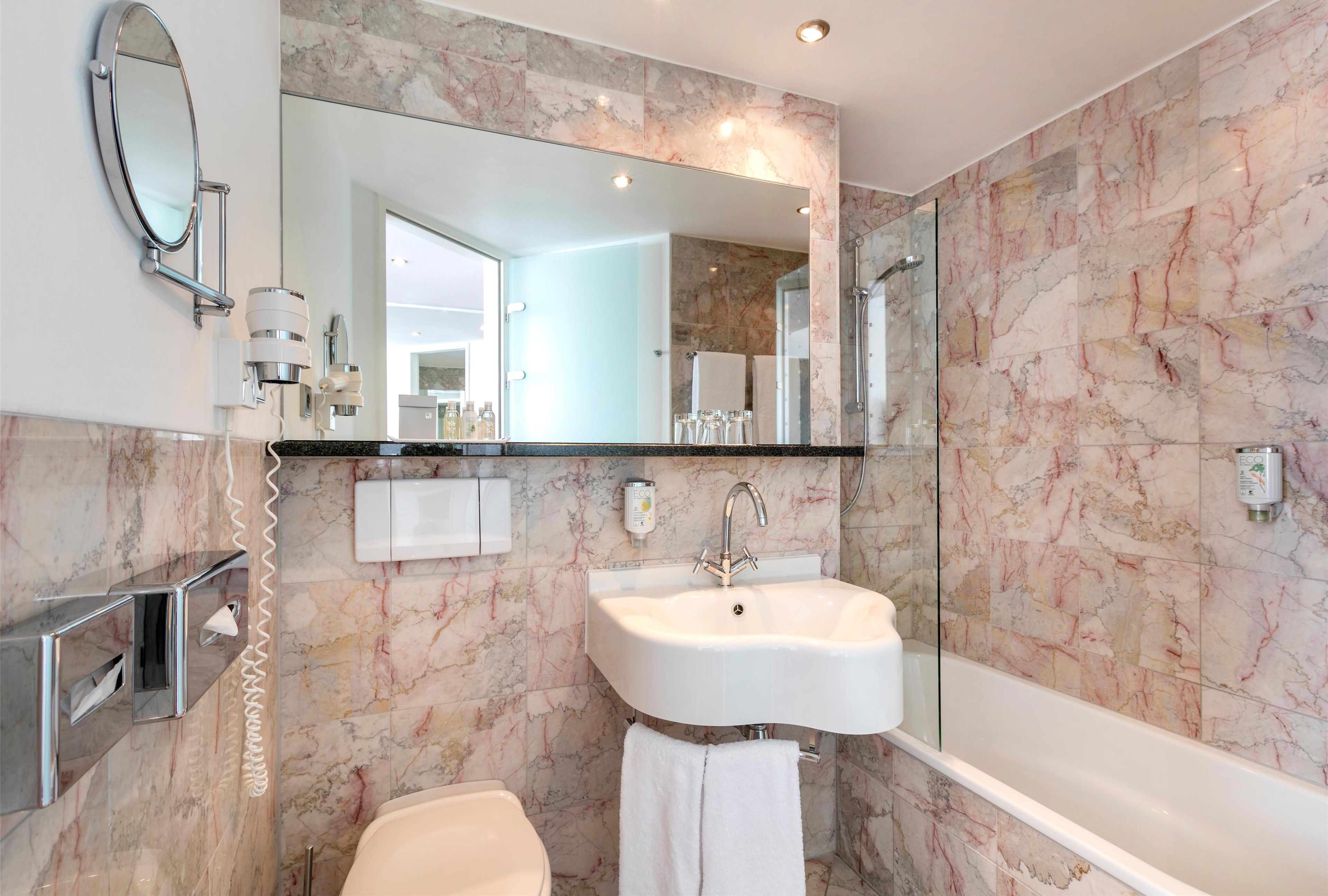 Un baño moderno con pared de mármol, lavamanos blanco, espejo y ducha con cerramientos de vidrio.