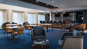 A modern hotel lobby with round tables, comfortable seating, a bar area, and a large TV screen. - Courtyard by Marriott San Antonio Airport (San Antonio)